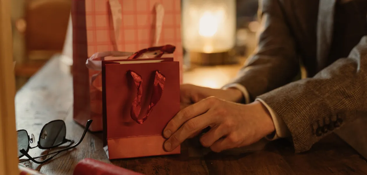 Hands arranging housewarming gift bags on a wooden table