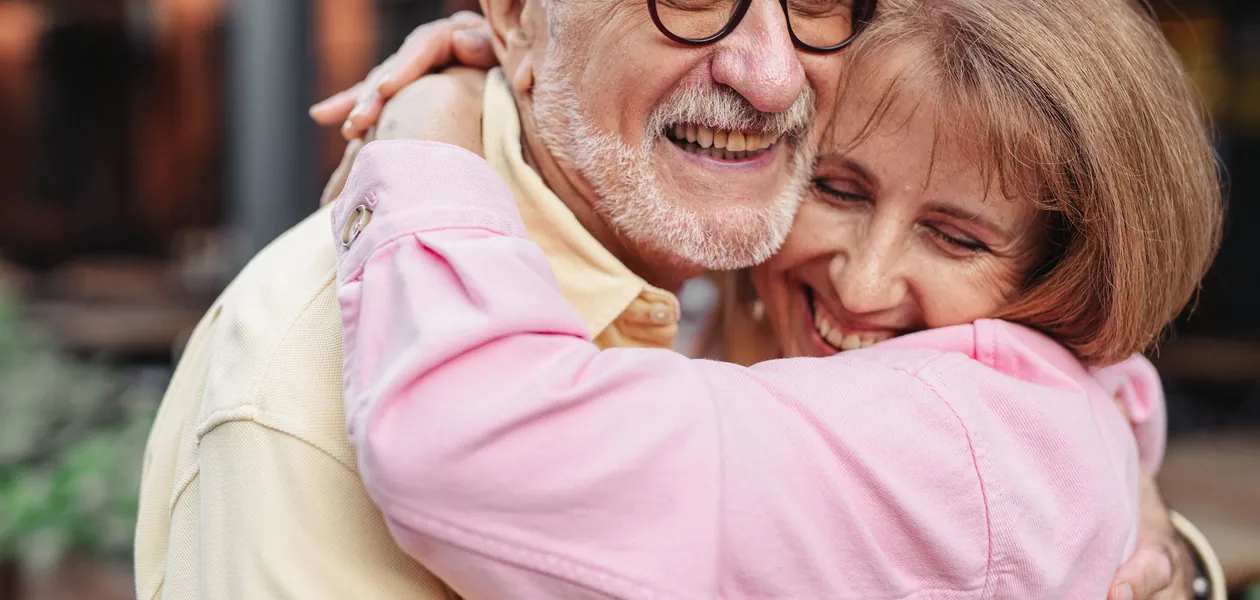 A joyful elderly couple sharing a warm embrace outdoors, exuding love and happiness.