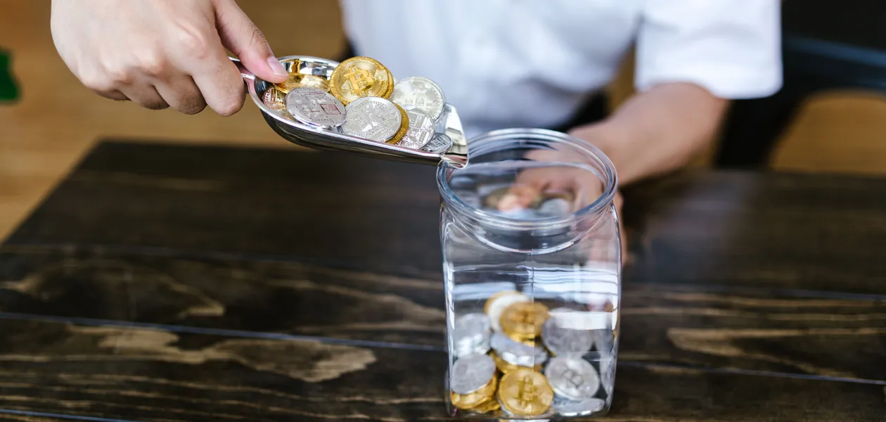 hand dropping coins into a glass on a wooden table
