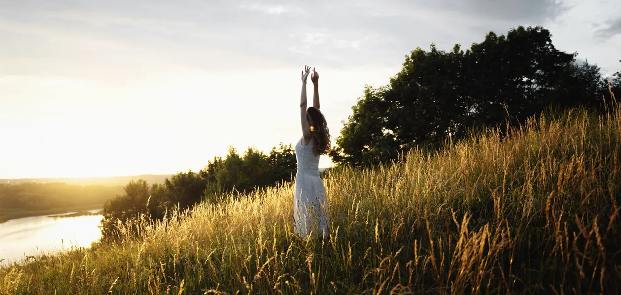 woman greeting the morning sun in an open field
