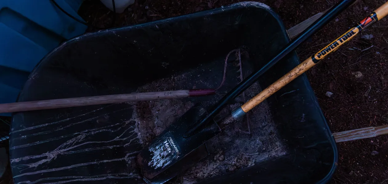 garden hand tools including a shovel and rake in a wheelbarrow
