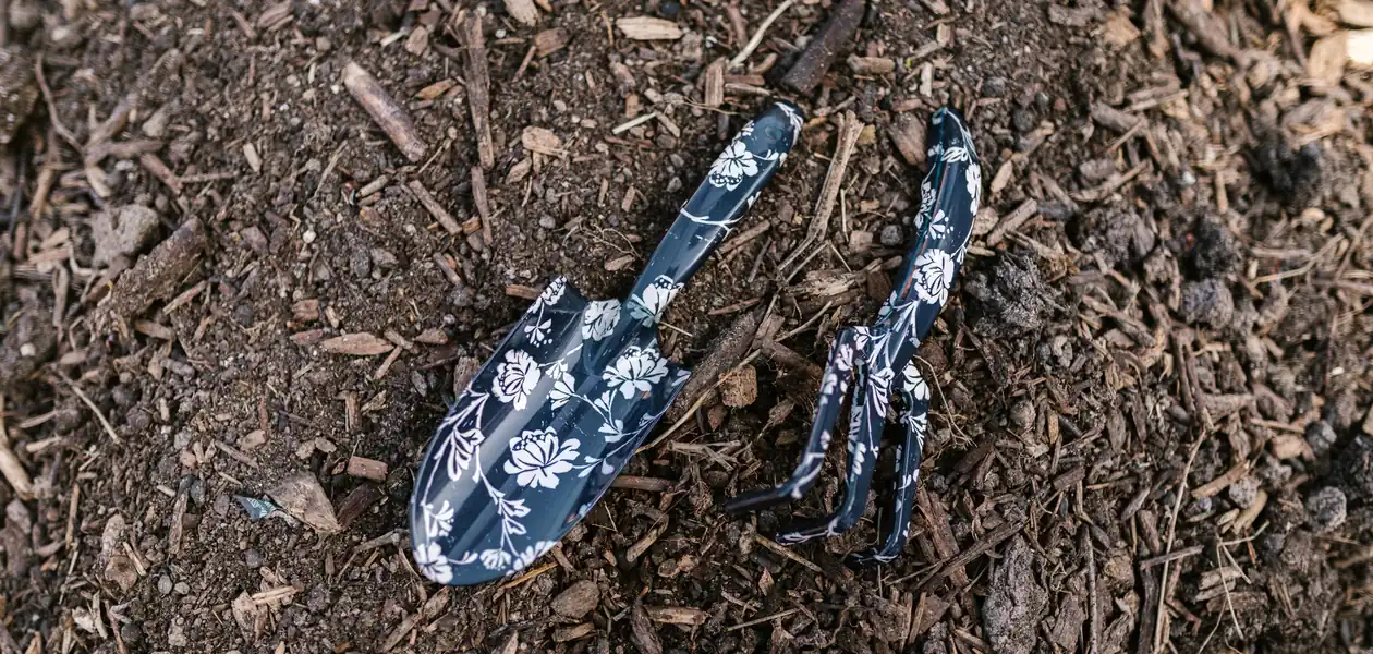 floral patterned trowel and hand tools resting on garden soil