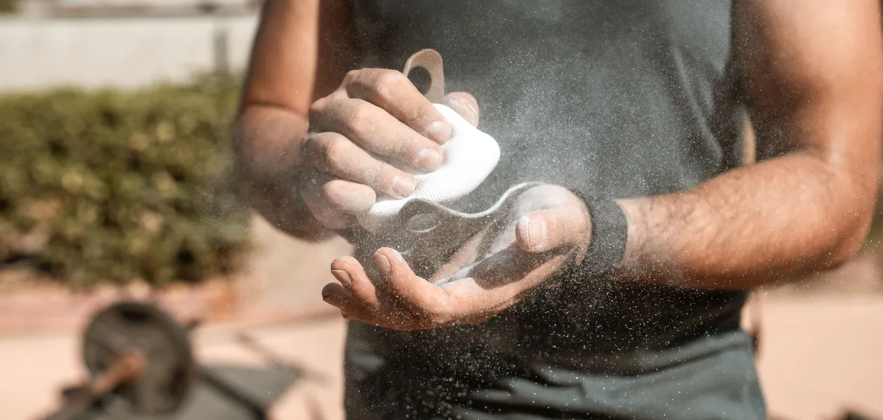 A man applies chalk to his hands during an outdoor weightlifting session, emphasizing fitness.