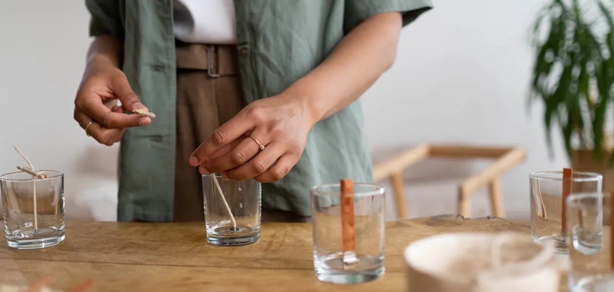 Hands crafting a scented candle in a glass jar on a wooden table
