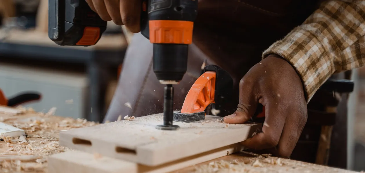 man using a cordless drill on a wood board in a home workshop