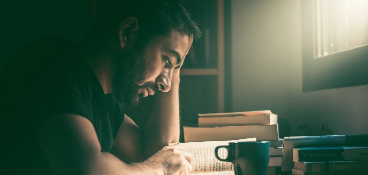 man reading a poker book by the window