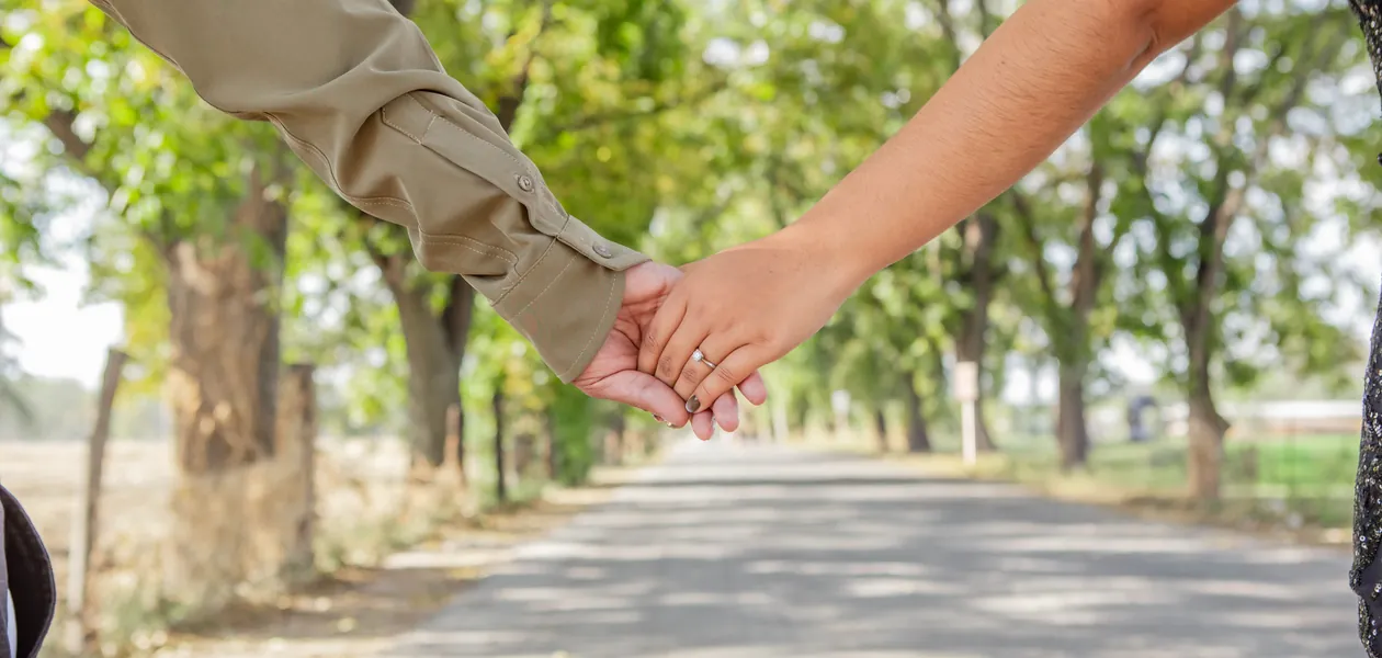 married couple walking hand in hand on a tree-lined road