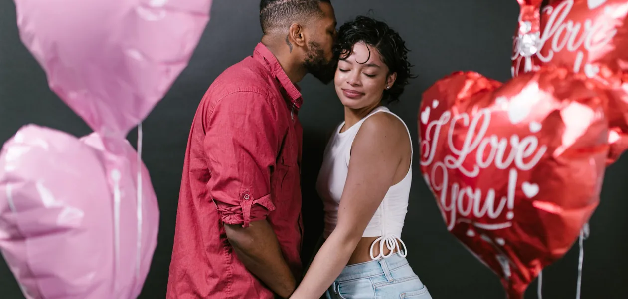 Romantic couple holding hands surrounded by heart-shaped balloons, celebrating love.