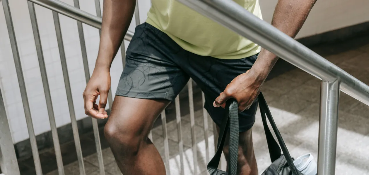 Man in athletic wear carrying a gym bag up a stairway, emphasizing fitness lifestyle.